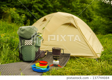 Colorful silicone camping tableware and stove set on a mat by a tent. Colorful silicone camping tableware and stove set on a mat by a tent. 137744084