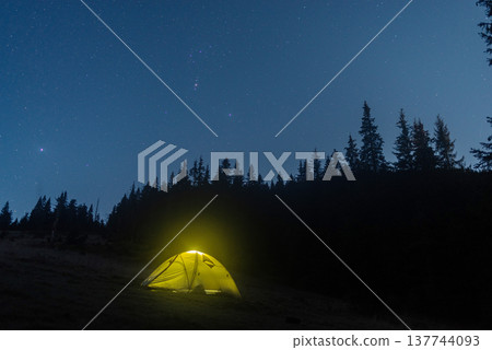 Illuminated camping tent under a starry night sky in the mountains. 137744093
