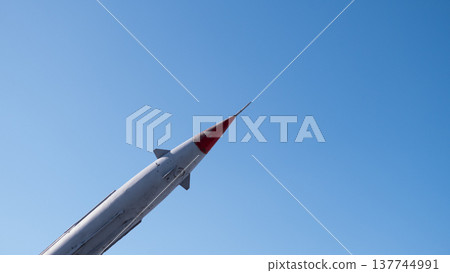 Rocket Poised For Launch Under Blue, Clean Vertical Stance With Red Nosecone And Service Hardware Visible, Pad Infrastructure Hinted, Countdown Preparedness Mood, Focus On Propulsion Systems Rocket Poised For Launch Under Blue, Clean Vertical Stance With Red Nosecone And Service Hardware Visible, Pad Infrastructure Hinted, Countdown Preparedness Mood, Focus On Propulsion Systems 137744991