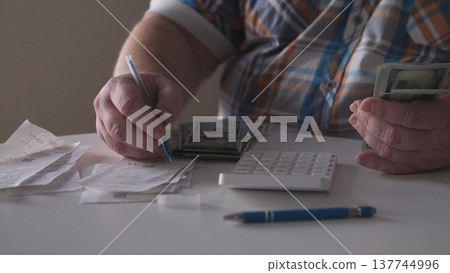 A person sits at a table counting cash and organizing receipts. They use a calculator to track expenses and manage their finances. The setting is bright and simple. A person sits at a table counting cash and organizing receipts. They use a calculator to track expenses and manage their finances. The setting is bright and simple. 137744996