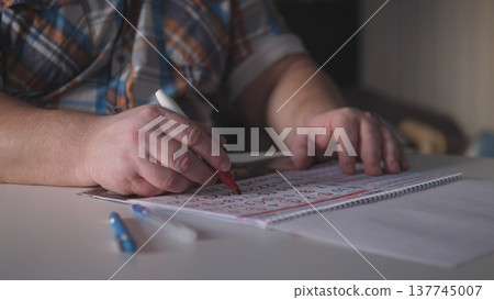 A person uses a red marker to write on a calendar while seated at a table. Several pens are placed on the table, showing an organized workspace in a brightly lit room. A person uses a red marker to write on a calendar while seated at a table. Several pens are placed on the table, showing an organized workspace in a brightly lit room. 137745007