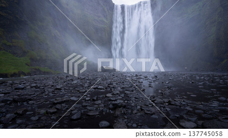 Huge waterfall shot from down below with small people for reference below it, Iceland Huge waterfall shot from down below with small people for reference below it, Iceland 137745058
