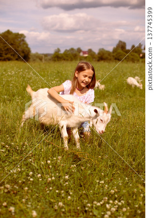 Girl cradling a baby goat in her arms, surrounded by a lush green field, basking in the warmth of a sunny day Girl cradling a baby goat in her arms, surrounded by a lush green field, basking in the warmth of a sunny day 137745399