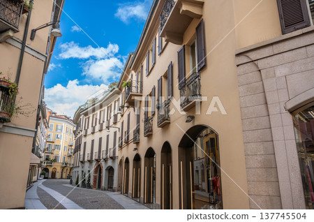 Milan, italy, april 1, 2024. Via della madonnina in milan brera: narrow cobblestone street lined with historic facades, boutiques and blue summer sky above Milan, italy, april 1, 2024. Via della madonnina in milan brera: narrow cobblestone street lined with historic facades, boutiques and blue summer sky above 137745504