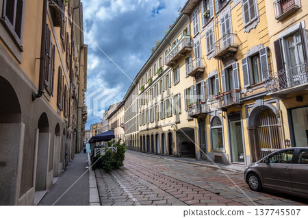 Milan, italy, april 1, 2024. Milan brera streetscape with traditional facades, cobblestone-paved road, sidewalk and a gray car parked on the right, sunny day Milan, italy, april 1, 2024. Milan brera streetscape with traditional facades, cobblestone-paved road, sidewalk and a gray car parked on the right, sunny day 137745507