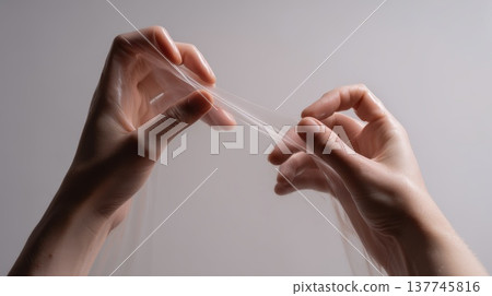 Hands stretching transparent slime material in studio light, tactile sensory texture showing elasticity and flexible polymer material 137745816