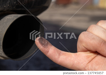 A man points out the grime on an exhaust pipe, emphasizing the need for cleaner emissions and proper vehicle care in a bustling neighborhood 137745857