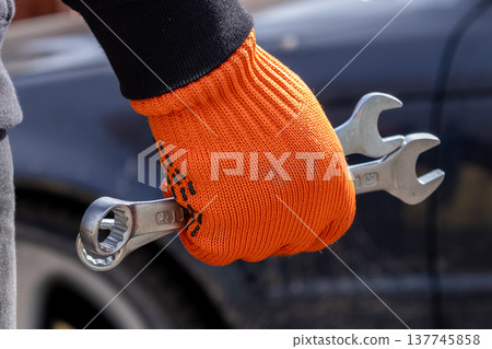 Mechanic grips metal keys tightly while standing by a car awaiting repair in a bright, sunny workshop setting 137745858