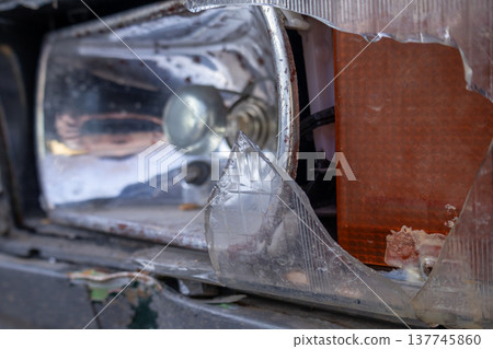 A shattered headlight unveils fragments of light and memories, resting quietly on an abandoned vehicle in a forgotten neighborhood A shattered headlight unveils fragments of light and memories, resting quietly on an abandoned vehicle in a forgotten neighborhood 137745860