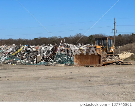 Heavy machinery sits idle near towering piles of waste at a bustling landfill under a clear blue sky, ready for action Heavy machinery sits idle near towering piles of waste at a bustling landfill under a clear blue sky, ready for action 137745861