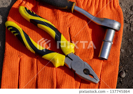 Brightly colored pliers and a socket wrench rest atop a sturdy orange glove, ready for car repair tasks in a busy workshop 137745864