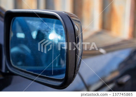 Glistening surface of a side mirror reveals intricate details and colors, showing a glimpse of a nearby artistic wood fence in soft morning light 137745865