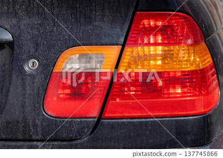 A car tail light illuminates in hues of red and amber, adding charm to the vehicle against a background of surface grime, captured on a sunny day 137745866