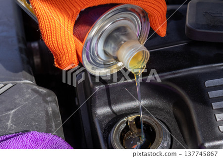 Mechanic carefully pours golden oil into the engine while sunlight shines on the vibrant tools and equipment scattered nearby Mechanic carefully pours golden oil into the engine while sunlight shines on the vibrant tools and equipment scattered nearby 137745867