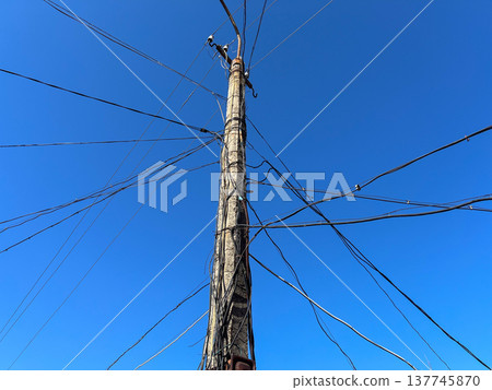 Concrete pole stands tall against the clear blue sky, adorned with a web of wires connecting the city's heartbeat and energy flow 137745870