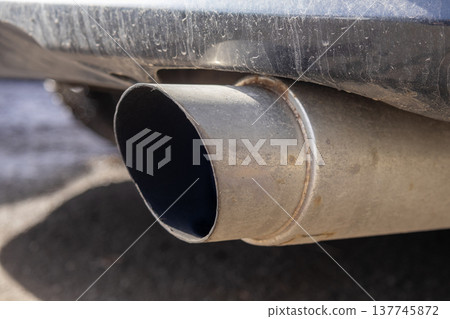 Exhaust pipe shows dirt and grime buildup, hinting at neglect, as the car sits idle on a warm day in a busy urban environment 137745872