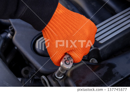 A man in an orange glove focuses intently on repairing a car engine, showcasing skill and dedication in a garage setting A man in an orange glove focuses intently on repairing a car engine, showcasing skill and dedication in a garage setting 137745877