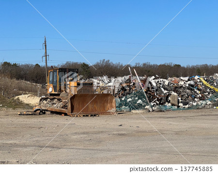 A powerful tractor clears debris at a busy landfill, shaping the landscape as it navigates through piles of waste in the bright afternoon light A powerful tractor clears debris at a busy landfill, shaping the landscape as it navigates through piles of waste in the bright afternoon light 137745885