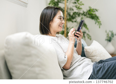 A young woman using her smartphone on the sofa at home. 137746702