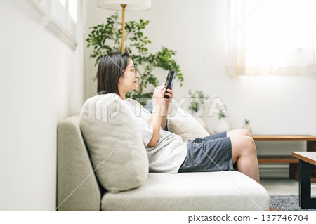 一位年輕女子在家裡的沙發上使用智慧型手機。 137746704