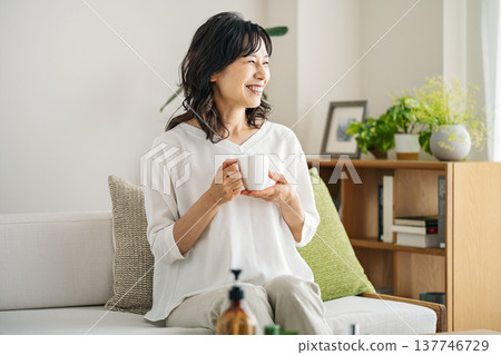 A middle-aged woman in her 50s relaxing on the sofa at home drinking coffee A middle-aged woman in her 50s relaxing on the sofa at home drinking coffee 137746729