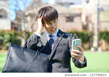 一位年輕的商人，看著他的智慧型手機，痛苦地抱住頭（上半身）。 137746814