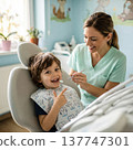 A cheerful little boy sitting in a dentist chair smiles brightly while a friendly female pediatric dentist performs a routine oral exam.. High quality photo 137747301