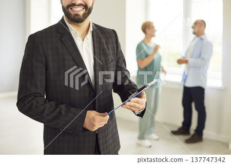 Smiling real estate agent with clipboard meeting couple in bright home together Smiling real estate agent with clipboard meeting couple in bright home together 137747342