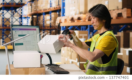 Asian employee using scanner to register shipping labels on cardboard boxes, professional tracking software to ensure express delivery. Online shopping large business tasks. Camera B. Asian employee using scanner to register shipping labels on cardboard boxes, professional tracking software to ensure express delivery. Online shopping large business tasks. Camera B. 137747401