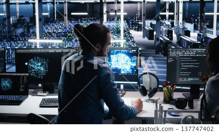 Teamworking engineers doing brainstorming in data center, reviewing AI diagnostics on computer. Team of IT expert working together in server room, optimizing artificial intelligence systems, camera A Teamworking engineers doing brainstorming in data center, reviewing AI diagnostics on computer. Team of IT expert working together in server room, optimizing artificial intelligence systems, camera A 137747402