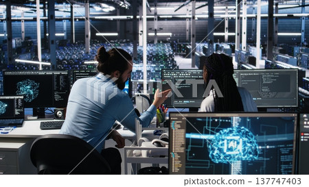 Data center coworkers having fun in office, using machine learning algorithms to analyze datasets. Server farm colleagues goofing around while using AI at work, workplace friendship concept, camera A 137747403