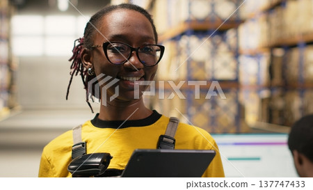 Employee using barcode scanner on cardboard boxes in fulfillment center. Organized shelving, package labels and route planning support efficient distribution and shipment. Logistics hub. Camera B. 137747433
