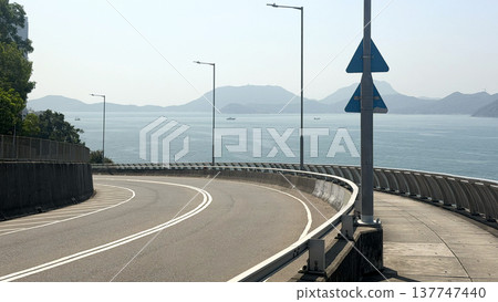 Curving highway overpass with ocean and distant mountains under clear sky Curving highway overpass with ocean and distant mountains under clear sky 137747440