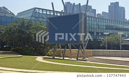 Large outdoor digital billboard screen mockup in a modern city park with glass buildings in the background 137747443