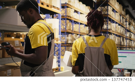Employee using barcode scanner on cardboard boxes in fulfillment center. Organized shelving, package labels and route planning support distribution and shipment. Logistics hub. Camera A. Employee using barcode scanner on cardboard boxes in fulfillment center. Organized shelving, package labels and route planning support distribution and shipment. Logistics hub. Camera A. 137747453