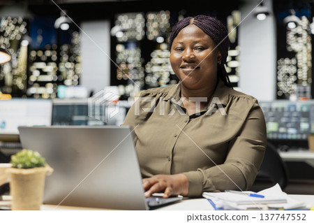Portrait of smiling analyst working after hours on finances at the office, fact checking numbers and data metrics. Organizing the agenda for upcoming administrative tasks, management. Portrait of smiling analyst working after hours on finances at the office, fact checking numbers and data metrics. Organizing the agenda for upcoming administrative tasks, management. 137747552