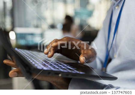 African American professional typing on laptop, inputting project data in office. Close up of fingers on keyboard, working on digital device to update financial analysis and research information. African American professional typing on laptop, inputting project data in office. Close up of fingers on keyboard, working on digital device to update financial analysis and research information. 137747603