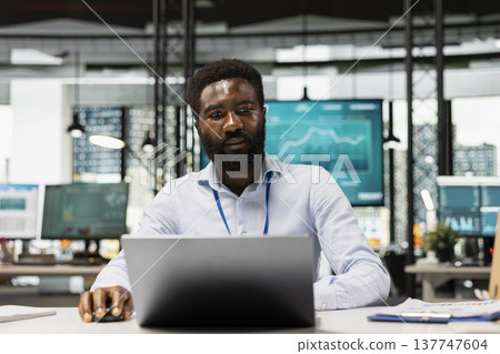 Focused black male employee in modern office, reading online files for project planning. African American accountant works at desk, developing financial plan for presentation in corporate workplace. Focused black male employee in modern office, reading online files for project planning. African American accountant works at desk, developing financial plan for presentation in corporate workplace. 137747604