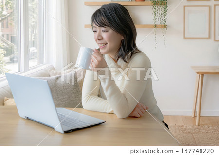 A woman drinking coffee and looking at her computer at home. A woman drinking coffee and looking at her computer at home. 137748220
