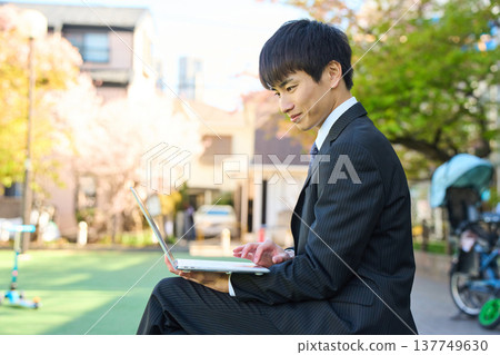 一位年輕的商人坐在公園長椅上用筆記型電腦工作（上半身） 137749630