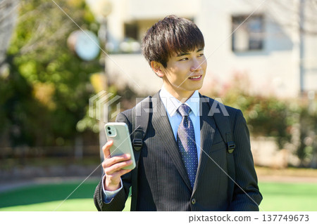 A new businessman in a park, wearing a backpack, checking maps and contacts on his smartphone (upper body). 137749673