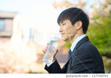 一位新晉商人正在公園裡喝瓶裝水提神。 (上半身,側面照) 一位新晉商人正在公園裡喝瓶裝水提神。 (上半身,側面照) 137749701