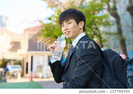 一位新晉商人外出拜訪客戶時,在公園裡補充水分,臉上露出笑容。 (上半身) 一位新晉商人外出拜訪客戶時,在公園裡補充水分,臉上露出笑容。 (上半身) 137749703