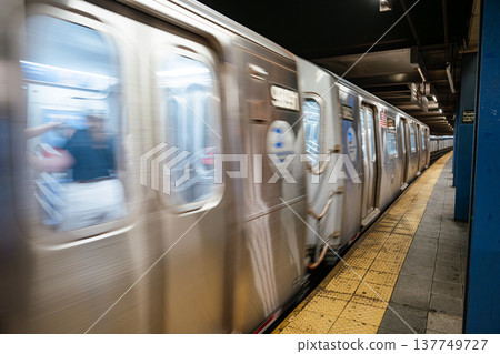 Blurred New York City subway train moving along the platform at Broadway Lafayette Street station. Underground urban transit system showing speed, stainless steel cars, and yellow safety strip. 137749727