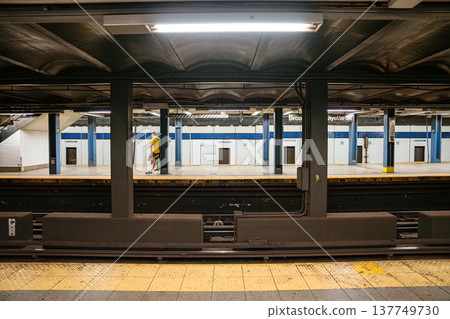 A commuter walks across the Broadway Lafayette Street subway platform in New York City. Underground metro station with tiled walls, steel beams, and urban public transportation setting. 137749730