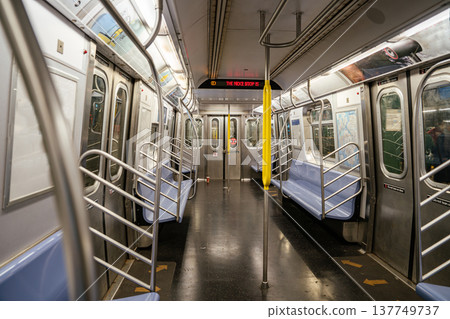 Empty New York City subway train interior showing digital next stop sign and stainless steel doors. Urban public transportation environment with yellow poles, blue seats, and modern metro design. Empty New York City subway train interior showing digital next stop sign and stainless steel doors. Urban public transportation environment with yellow poles, blue seats, and modern metro design. 137749737