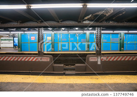 New York City subway platform at West 4 Street station with blue construction panels and safety markings across the tracks. Urban underground metro scene with railway infrastructure, steel columns 137749746