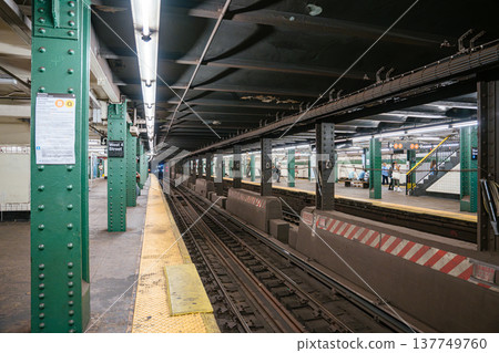 Subway tracks run through West 4 Street station in Manhattan. Green steel columns and yellow platform edge highlight New York City public transportation infrastructure. 137749760