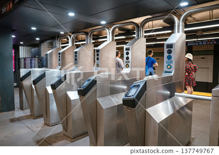 Metal subway turnstiles stand inside a New York City subway station. Commuters use public transportation in Manhattan's underground transit system. Metal subway turnstiles stand inside a New York City subway station. Commuters use public transportation in Manhattan's underground transit system. 137749767