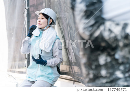 建築工地採取中暑預防措施。一名女油漆工穿著降溫背心休息，並持續補充水分。 137749771